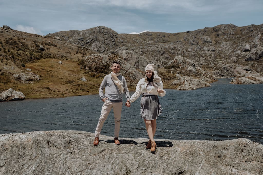 Janner y Marcela de la mano sobre una roca, con la laguna y las montañas del páramo detrás